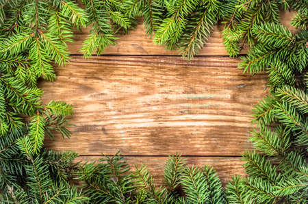 Christmas tree twigs of spruce on a wood background arranged in frame pattern useful as holiday background in vintage style.の写真素材