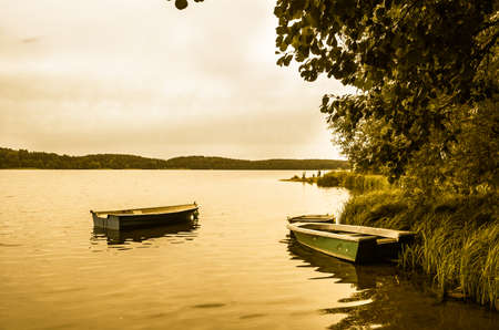 Landscape stylized on vintage with boats for fishing on the lake at the shore. Vintage photo. Nature background. Tranquil landscape.の写真素材