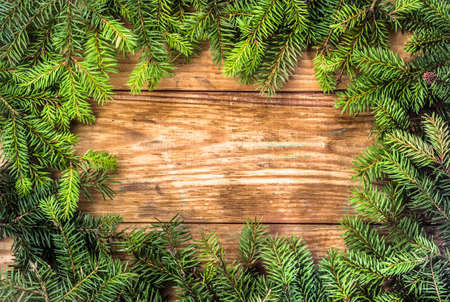 Christmas tree twigs of spruce on a wood background arranged in frame pattern useful as holiday background in vintage style.の写真素材