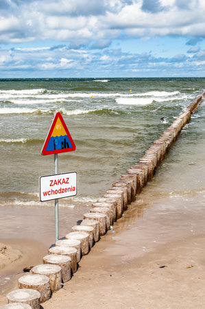 Landscape of sea with waves and cloudy sky. Breakwater and warning sign in the foreground. Baltic sea coast near Leba in Poland.の写真素材