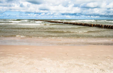 Landscape of beach and sea with waves, cloudy sky, breakwater. Baltic sea coast near Leba in Poland.の写真素材