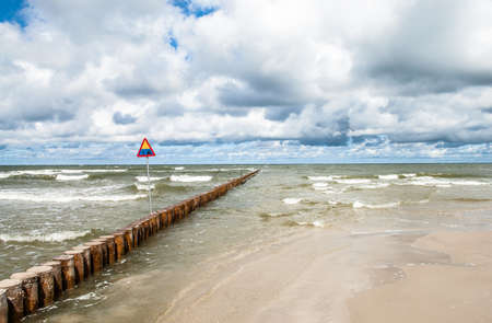 Landscape of sea with waves and cloudy sky. Breakwater and warning sign in the foreground. Baltic sea coast near Leba in Poland.の写真素材