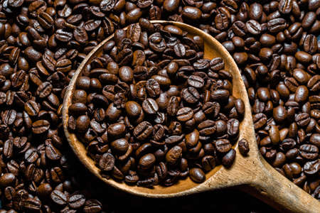 Freshly roasted coffee beans in wooden scoop. Black coffee background.の写真素材