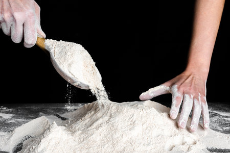 Baker pouring flour with a wooden spoon on kitchen table. Preparing dough for bread or pizza. Baking concept.の写真素材