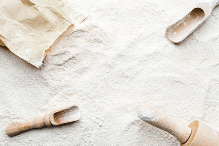 Background with flour. Rolling pin, wooden spoon, paper bag and flour, flat lay, top view.の写真素材