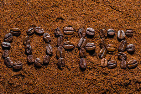 Background with coffee. Text made of freshly roasted beans arranged on powdered coffee, texture.の写真素材