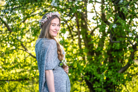 Smiling blonde girl with braid hairstyle and flower crown on her head posing in green garden.の写真素材