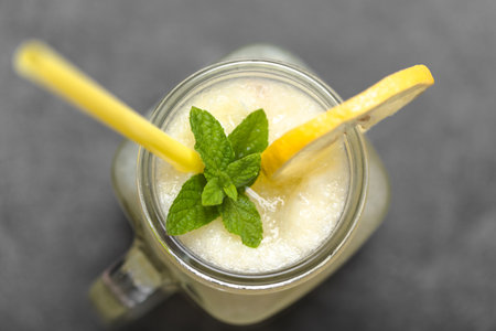 Fresh summer drink with straw. Jar glass of lemonade with lemons and mint on dark background.の写真素材