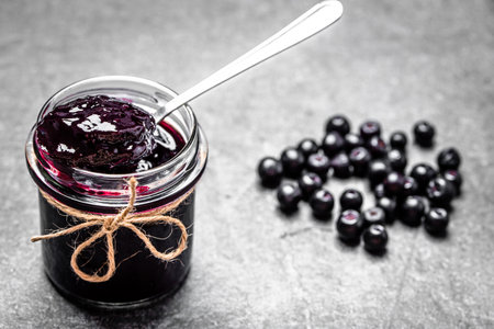 Aronia jam and fresh berry on stone table.