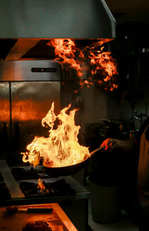 Cook holding flaming pan and flames rising from panの写真素材