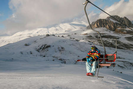 Snowboarder climbing up the hill, snow covered mountain landscape in the backgroundの写真素材