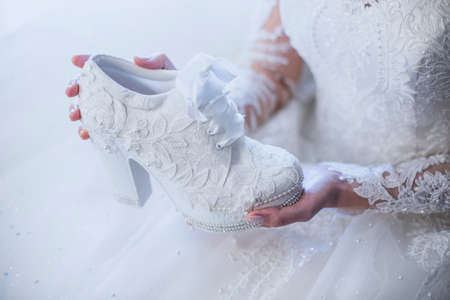 The bride is holding a white lace bridal shoe in her hands