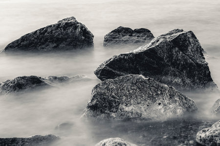Long exposure black and white photo of rocks and waves by the sea