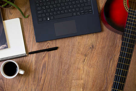 Red-black classical guitar standing on wooden floor, next to computer, phone and notebook-pen
