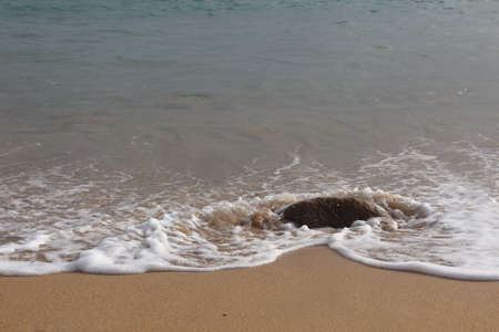 Wave on the beach passing a rockの写真素材