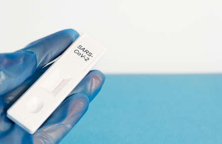 Antigen test concept for the COVIC-19 cororavirus. The doctor's blue-gloved hands hold the test, waiting for the result, on a white and blue background.の写真素材