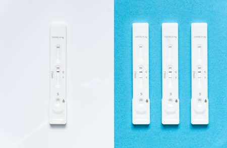Covid-19 / SARS-CoV-2 concept antigen rapid test, Omicron variant: 4 rapid test kits, one showing a negative result on white background (C) and three with a positive result on blue background (CT). Increased number of infections.の写真素材