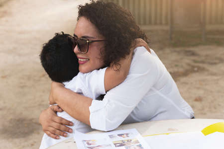 Latin single mother and son cuddling affectionately on a park bench one spring-summer afternoon.