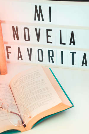 Close-up. Light box with message for International Book Day, next to it lined books and an open book with a pair of glasses on it, on the bedside table in the bedroom.の写真素材