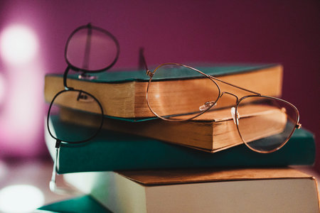 Close-up, pile of books with glasses between them on the bedside table next to the bed against the purple background of the wall.の写真素材