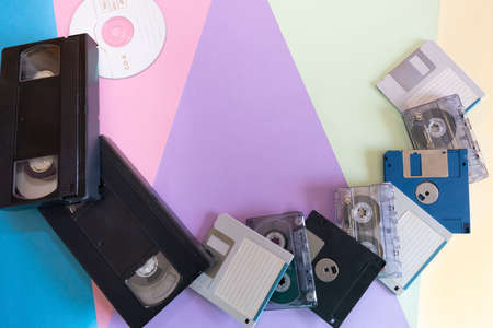 Whole plane, background depicting elements of the 1990s.Coloured cardboard creating triangular shapes and electronic storage devices, floppy disks, VHS tapes, cassettes and CDs.