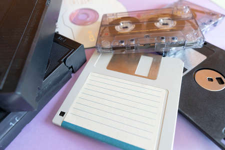 Close-up, background depicting elements of the 1990s. Colored cardboard creating triangular shapes and electronic storage devices, floppy disks, VHS tapes, cassettes and CDs.