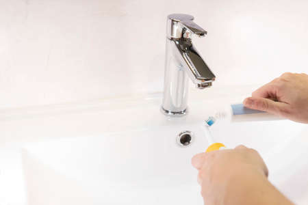 Medium close-up, woman putting toothpaste on electric toothbrush. Detail of the concept of oral...