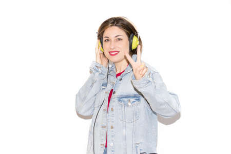Portrait of cheerful and pretty young woman smiling listening to music with green headphones on white background, with positive gesture of victory. Very colorful casual clothes and accessories.の写真素材