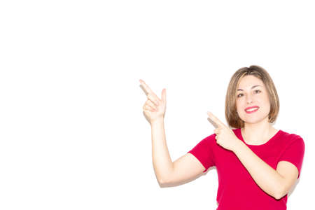 Horizontal photo of an adorable young woman dressed in casual pink clothing pointing to the empty blank space in the background, looking at the viewer.の写真素材