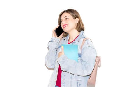 Young caucasian female student isolated on a white background talking on the phone in a cheerful conversation, while holding a book with the other arm. Lifestyle, spring.の写真素材
