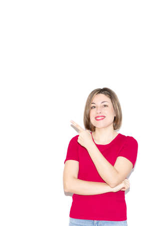 Vertical photo of an adorable young woman dressed in casual pink clothing pointing to the empty blank space in the background, looking at the viewer.の写真素材