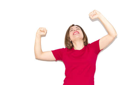 Image of a young woman celebrating a victory, bob haircut and casual fuchsia T-shirt isolated on a white background.の写真素材