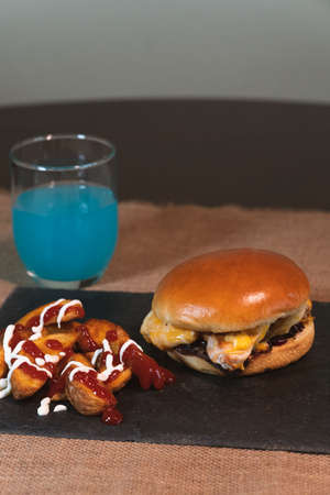 Turkey burger with ketchup and mayonnaise on a slate board and tropical fruit drink. Grilled turkey, caramelized onion and two types of cheese.の写真素材