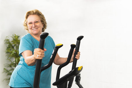 A woman is smiling while holding the handlebars of a stationary bike. Wearing a blue T-shirtの写真素材