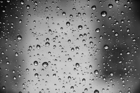 Black and white photo of raindrops on window glass.の写真素材