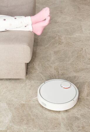 Stock photo of a robot vacuum cleaner cleaning the room while woman relaxing on sofaの写真素材