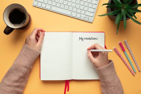 Stock photo of a young woman hands writing in a 2020 new year notebook with list of resolutions and objects on yellow backgroundの写真素材