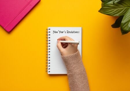 Stock photo of a young woman hand writing in a 2020 new year notebook with list of resolutions and objects on yellow backgroundの写真素材