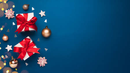 Merry Christmas and Happy Holidays greeting card background with copyspace on the right. Christmas gifts and golden decor on blue background top view. Winter xmas holiday theme in flat lay styleの写真素材