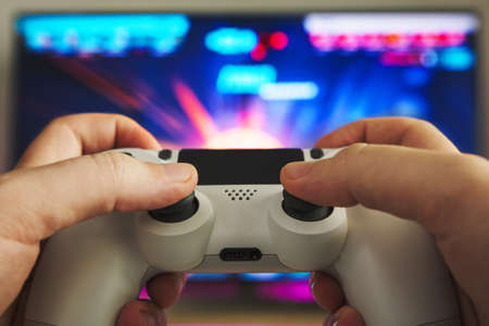 Stock photo of some hands with a gamepad playing a shooter game on the game console