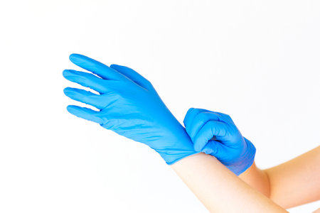 Stock photo of a woman's hands putting on blue latex gloves on a white backgroundの写真素材