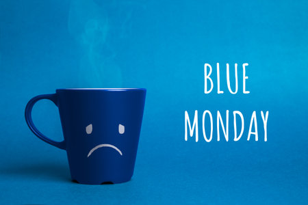 Stock photo of a blue cup on a blue background with a sad face drawn. Blue monday conceptの写真素材