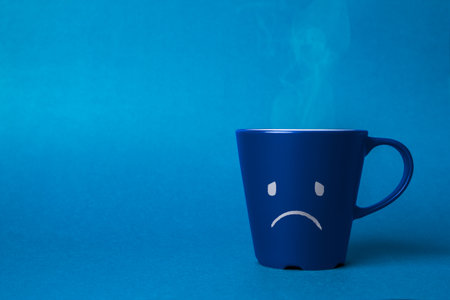 Stock photo of a blue cup on a blue background with a sad face drawn. Blue monday conceptの写真素材