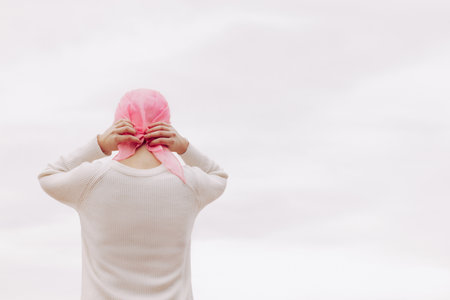 Stock photo of a young woman on her back placing a pink handkerchief on her head because she has...