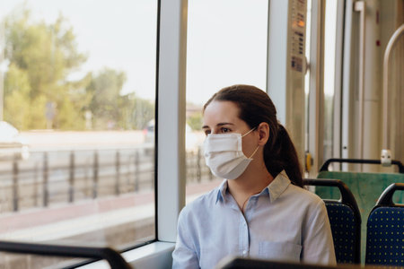 Stock photo of a young woman wearing a face mask traveling by tram. She is looking out the window. New normal conceptの写真素材
