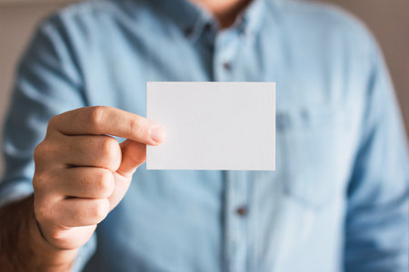 Empty paper business card mockup held by a man's hand, closeup. Logo and branding design template conceptの写真素材