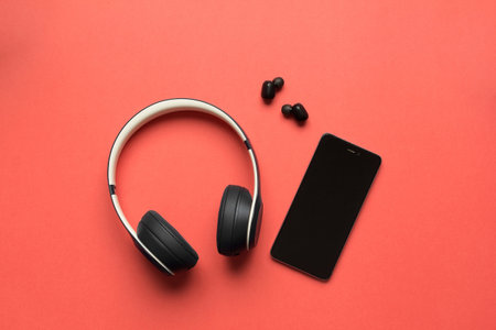 Stock photo of a big and small wireless headphones and a smartphone to listen to music on a red backgroundの写真素材