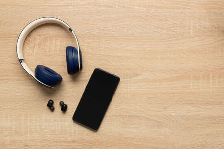 Stock photo of a big and small wireless headphones and a smartphone to listen to music on a wooden background and space for copy text at rightの写真素材