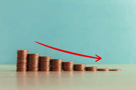 Stock photo of an descending staircase of coins on a blue background with a red arrow