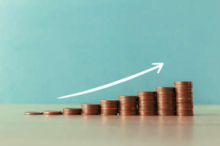 Stock photo of an ascending staircase of coins on a blue background with a white arrowの写真素材
